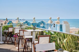 Una terraza con sillas y mesas de madera, con vista a una playa y al mar.