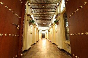 A hallway with a wooden door on the left, a tiled floor, and a ceiling with a patterned design. - Delmon International Hotel (Manama)
