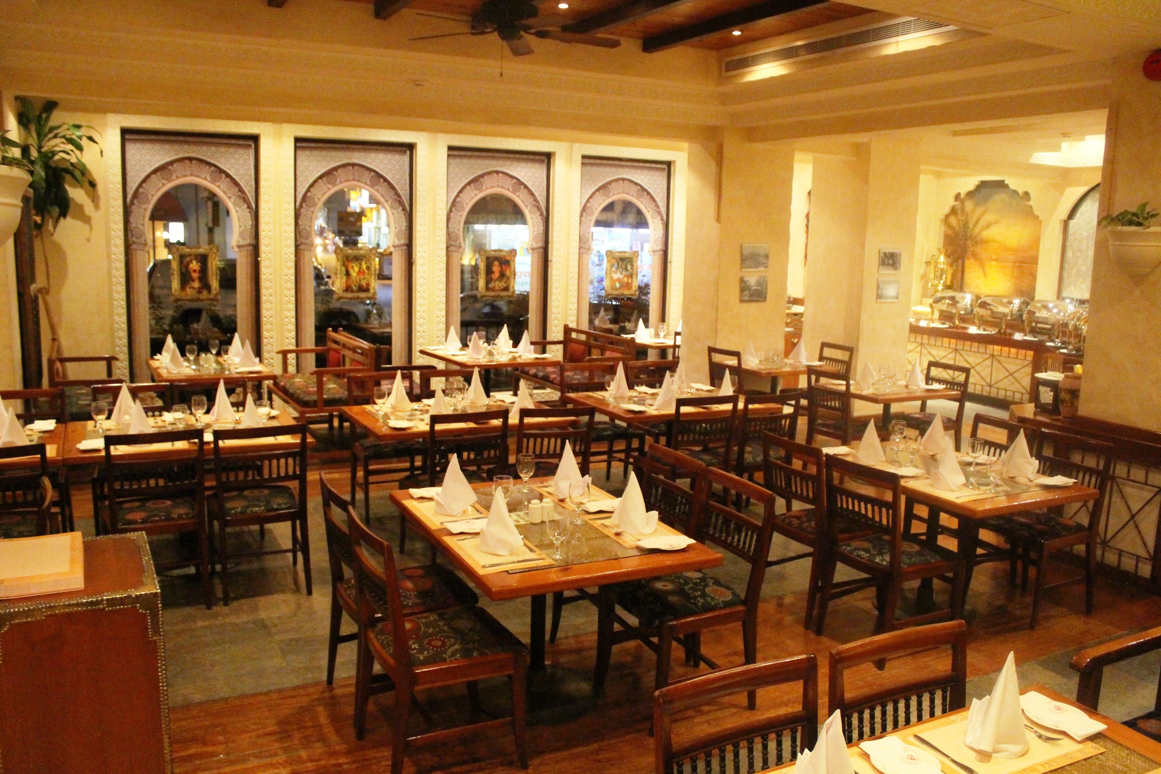 Un restaurante con varias mesas y sillas, cada conjunto con servilleta blanca, cristalería y cubiertos.