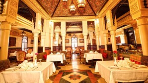 A restaurant with ornate ceiling and walls, multiple tables, and chairs arranged for dining. - Delmon International Hotel (Manama)
