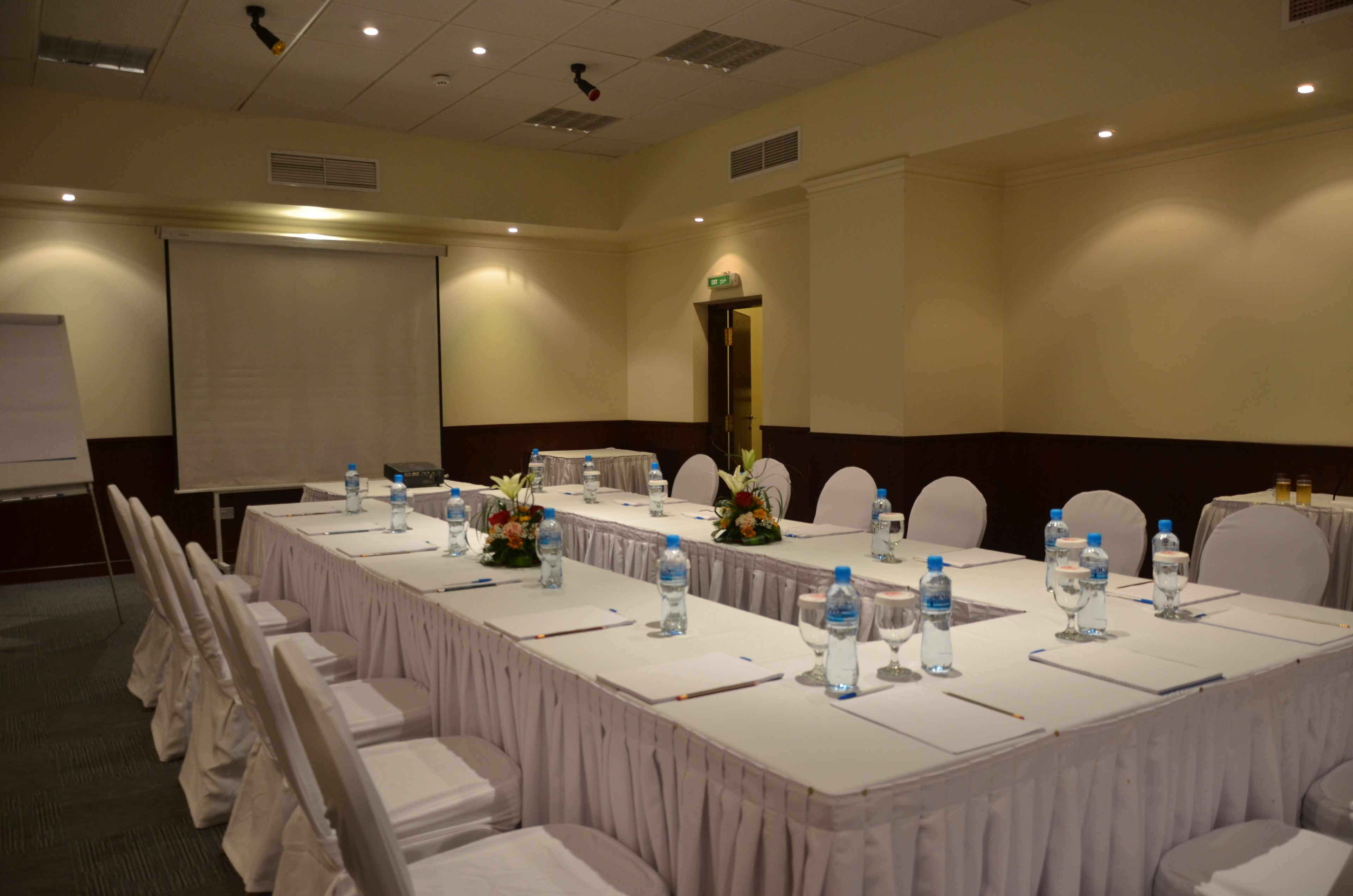 A conference room with a long table, chairs, water bottles, and a projector screen.