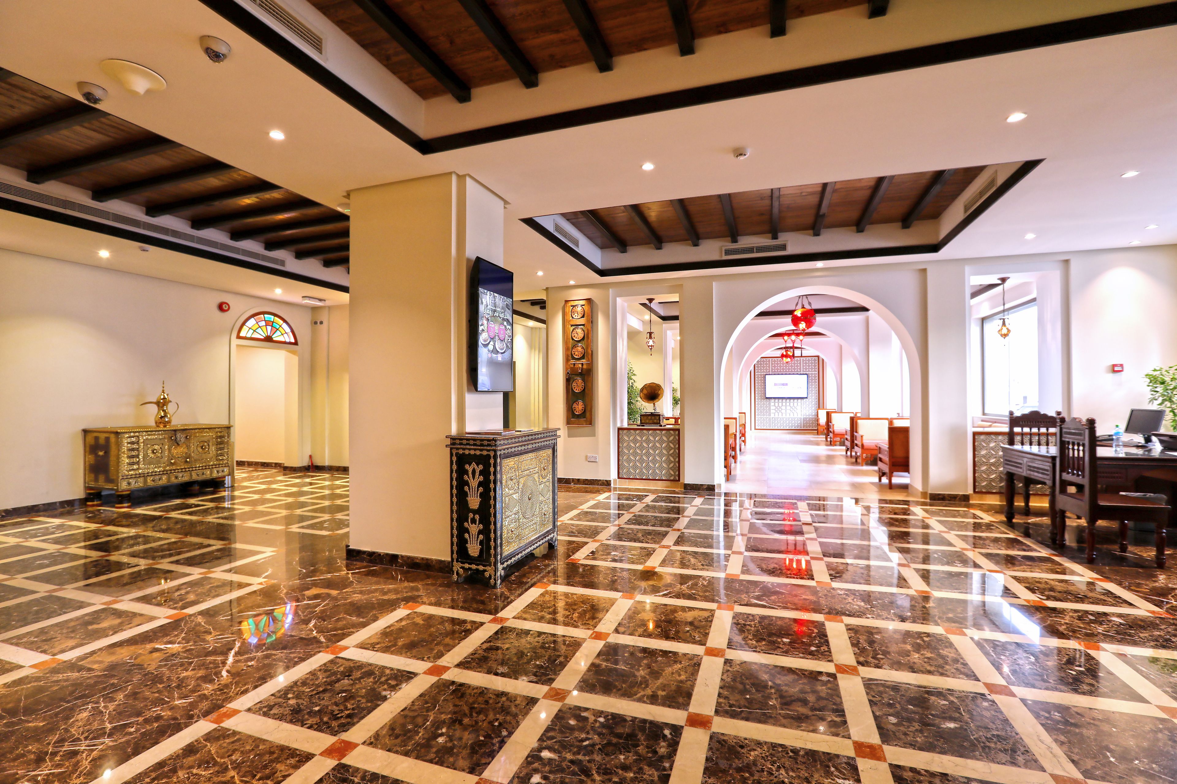 A spacious lobby with a checkered marble floor, a reception desk, and a dining area with chairs and tables.