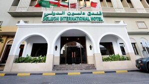 The exterior of the Delmon International Hotel with a prominent entrance, multiple flags, and a clear view of the entrance area. - Delmon International Hotel (Manama)