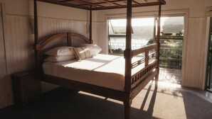 A four-poster bed with a wooden headboard, a nightstand, and a view of a balcony with a railing. - Cliff Edge by the Sea (Opua)
