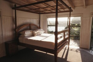 A four-poster bed with a wooden headboard, a nightstand, and a view of a balcony with a railing.
