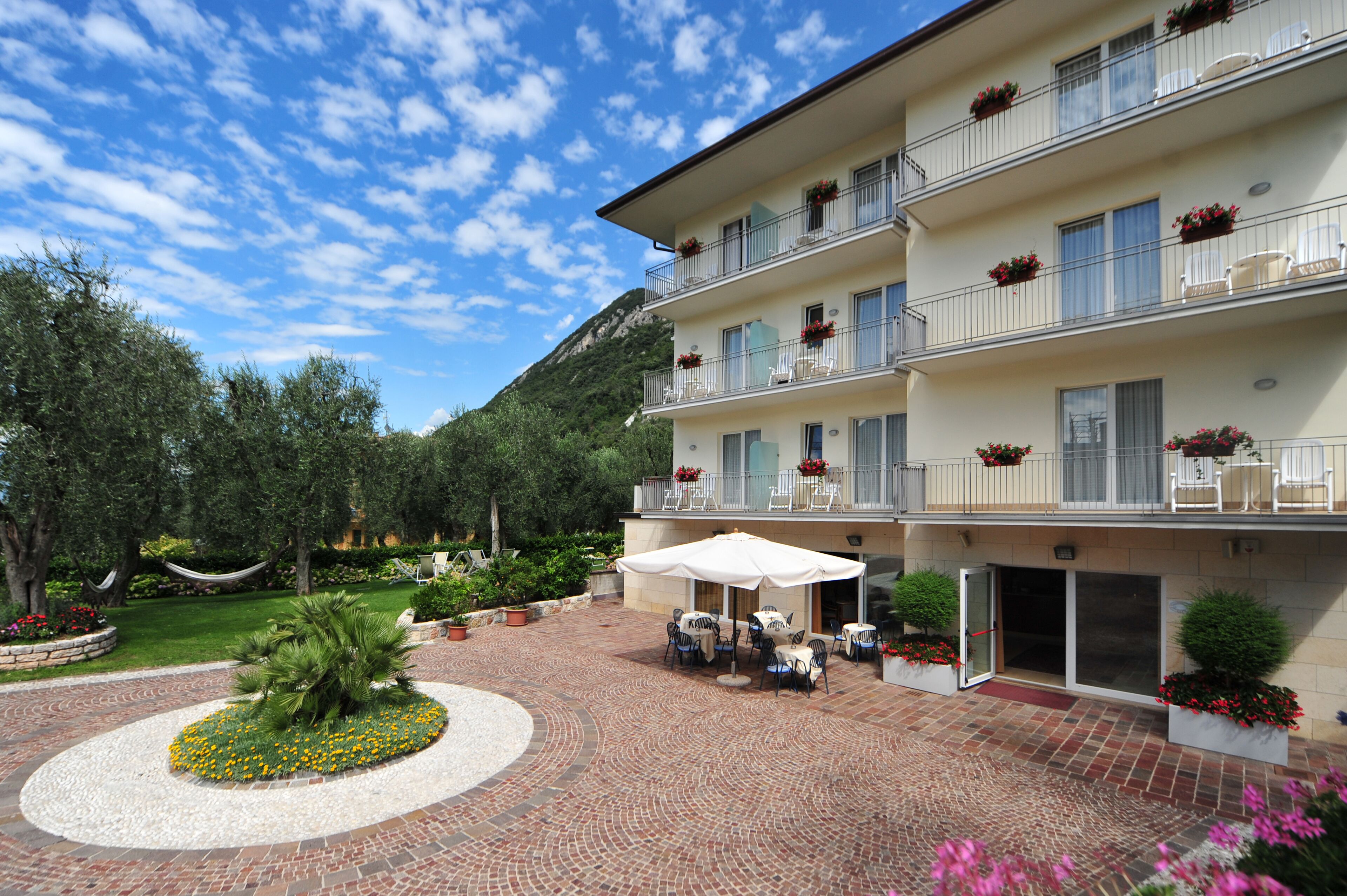 A multi-story hotel with outdoor seating, a garden, and a mountain backdrop.
