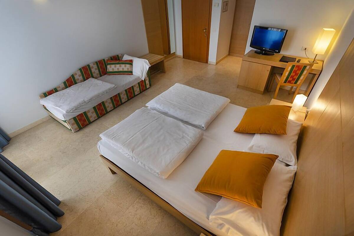 Une chambre d’hôtel avec deux lits simples, un canapé-lit, un bureau avec un ordinateur et une télévision.