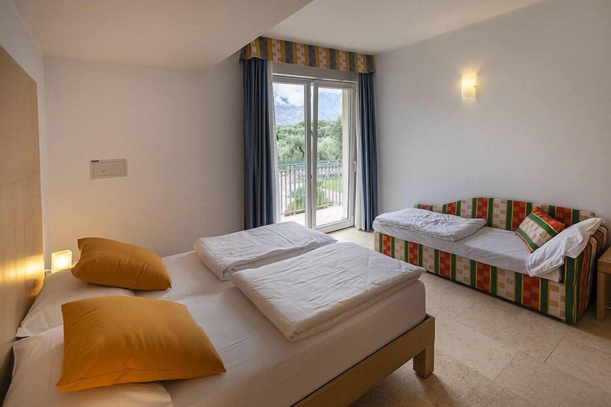 Une chambre avec deux lits, un canapé, une porte-fenêtre coulissante donnant sur un balcon et un luminaire fixé au mur.