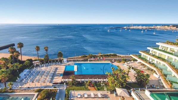 A resort with a large pool, sun loungers, and a view of the sea.