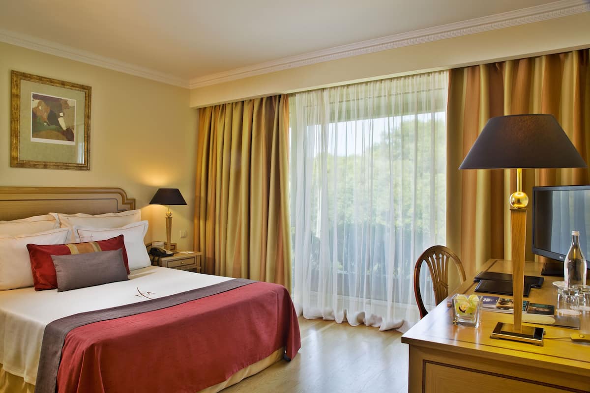 Una habitación de hotel con una cama bien hecha, un escritorio con lámpara, una silla y un televisor.