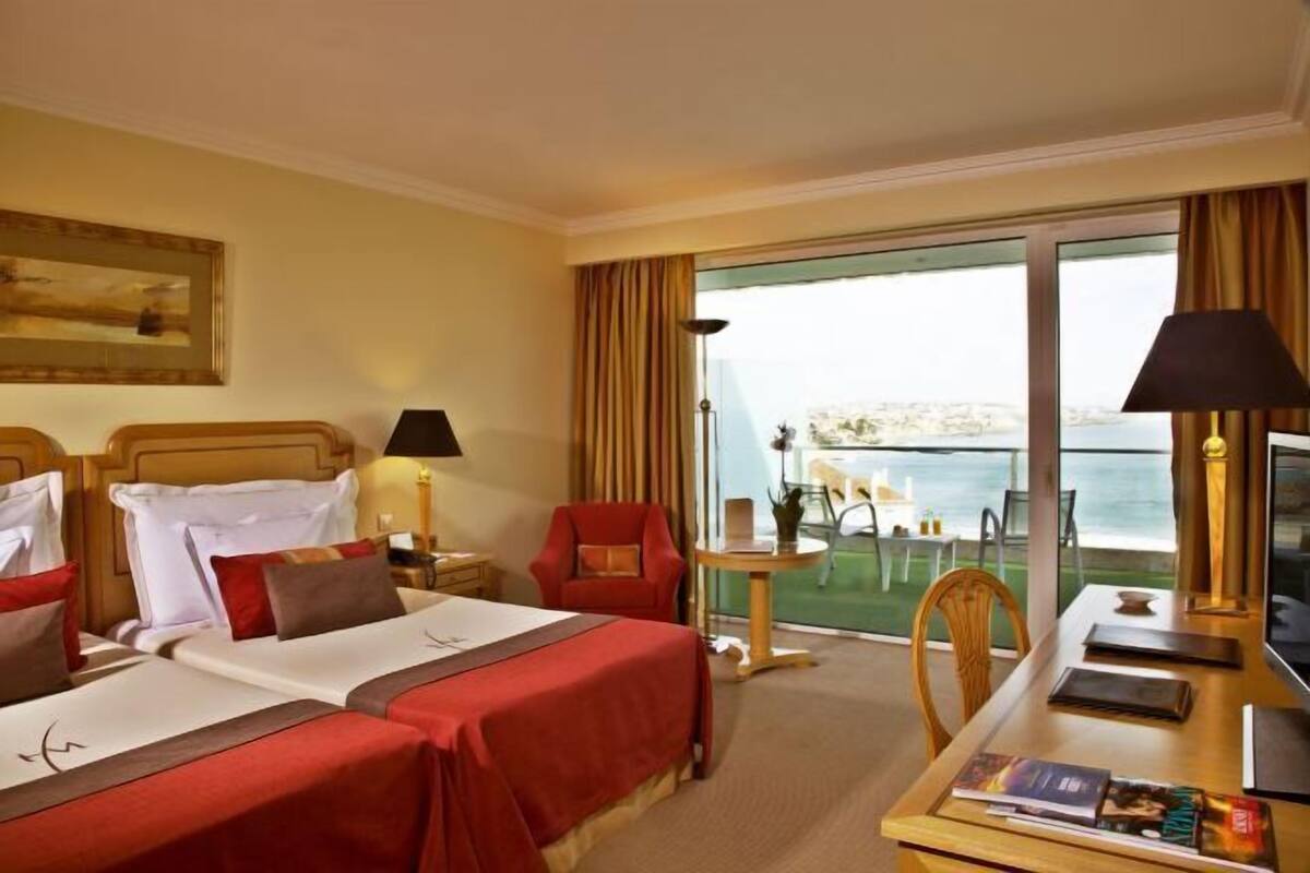 Habitación de hotel con dos camas, un escritorio, una silla, una mesa y vista al mar.