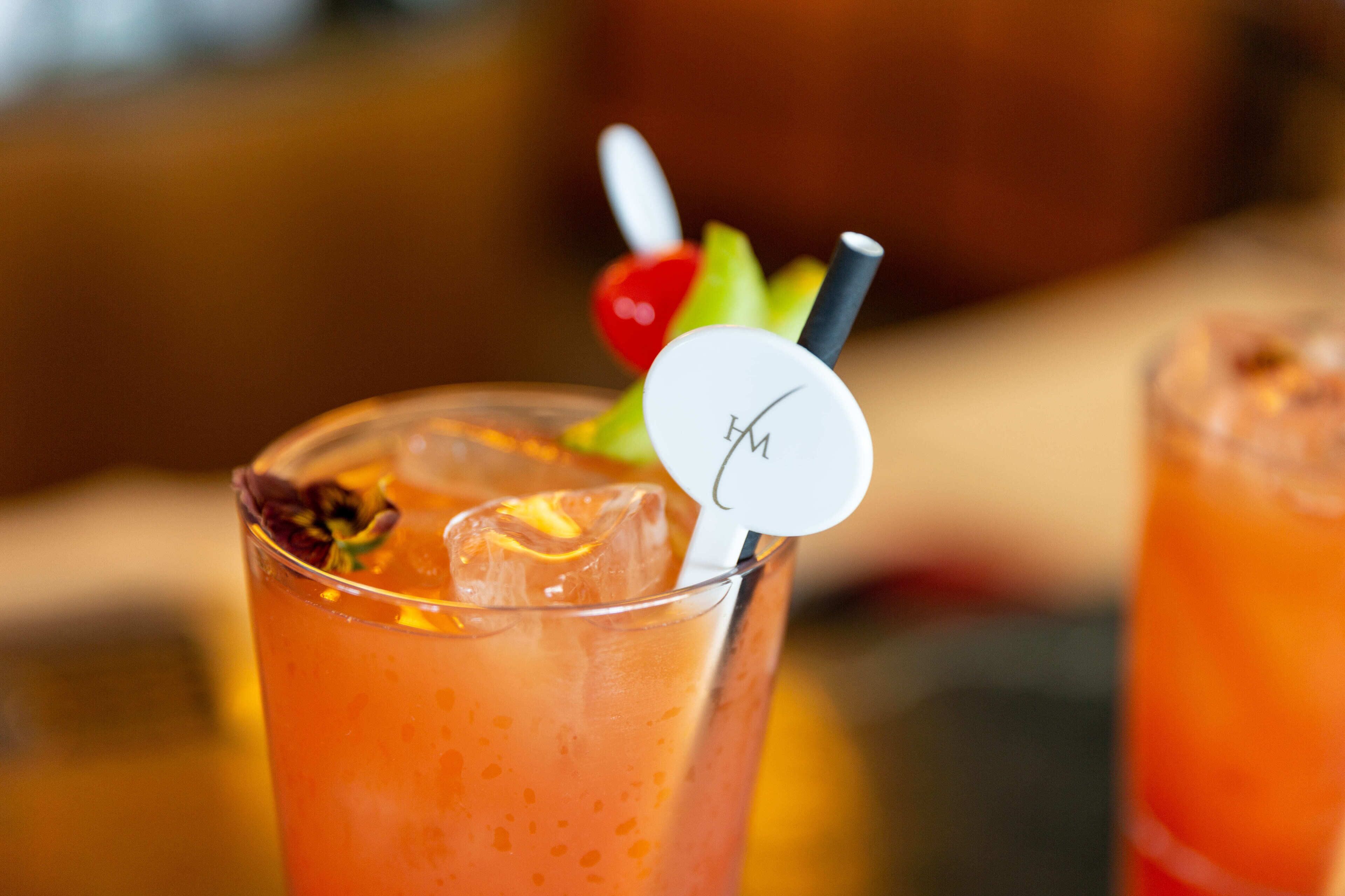 A glass of orange-colored beverage with a straw and a decorative item on the rim.