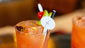 A glass of orange-colored beverage with a straw and a decorative item on the rim.
