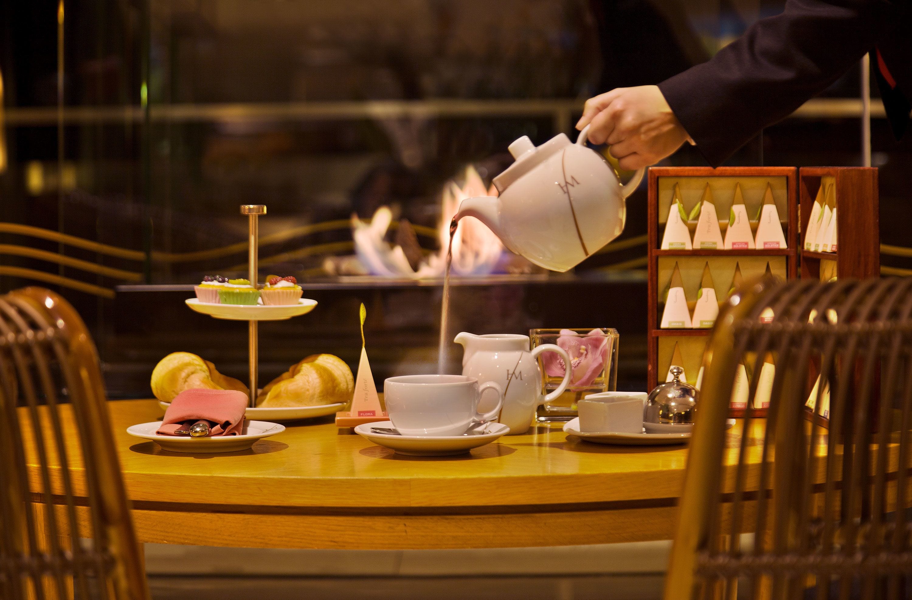 Una mesa dispuesta con tetera, tazas, un pastel pequeño y una exhibición de velas.