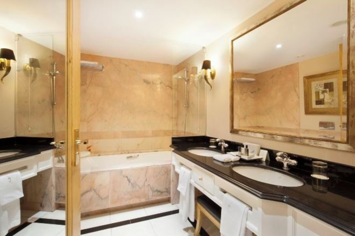 Een badkamer met twee wasbakken, een badkuip en een douche met glazen wanden.