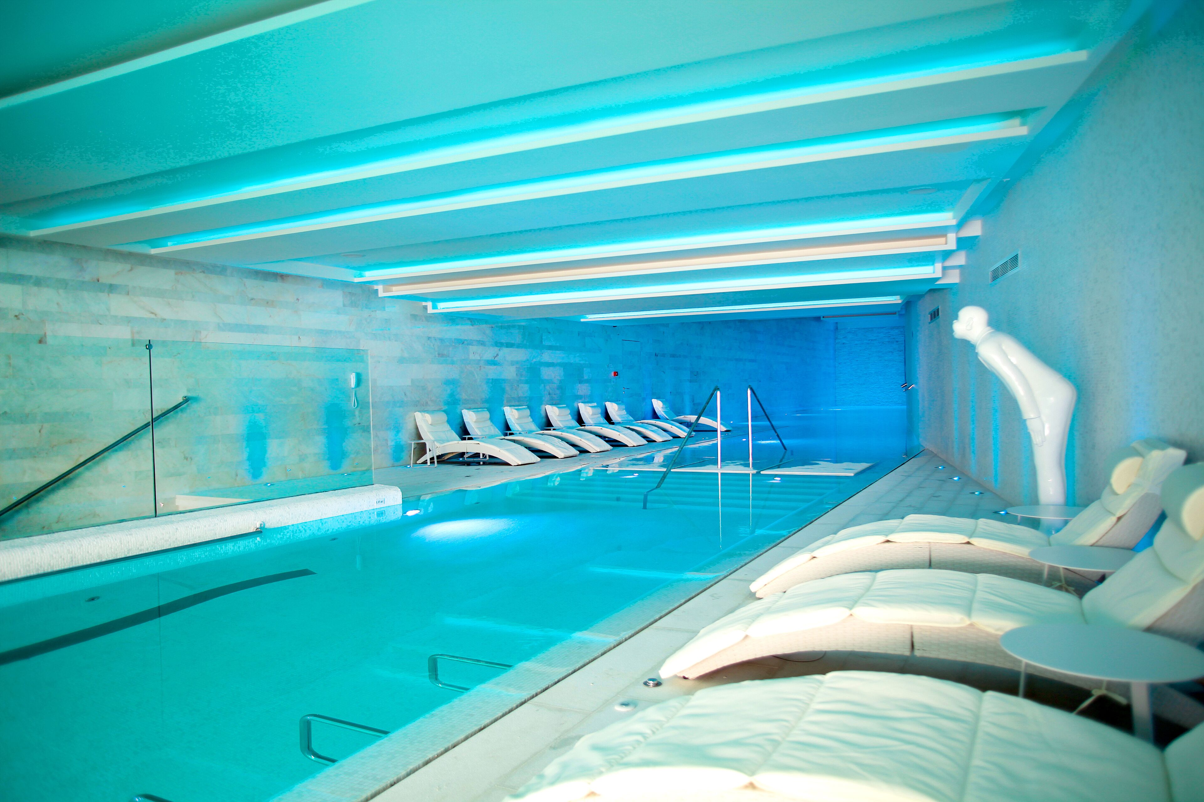 A swimming pool with lounge chairs and a ceiling with blue lighting.