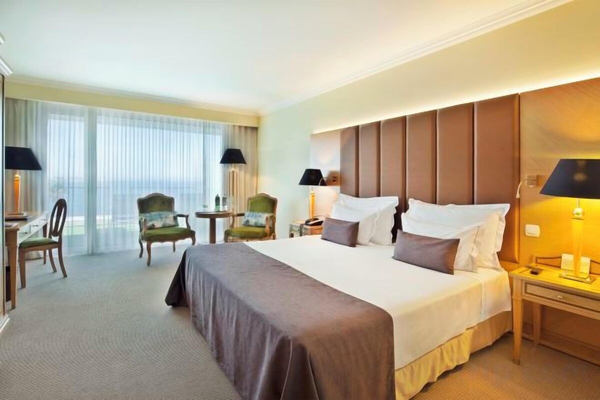 Une chambre d’hôtel avec un grand lit, deux tables de chevet, une chaise, un bureau et une vue sur l’extérieur.
