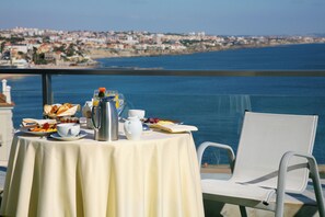A table set with breakfast items and a view of the sea and cityscape.