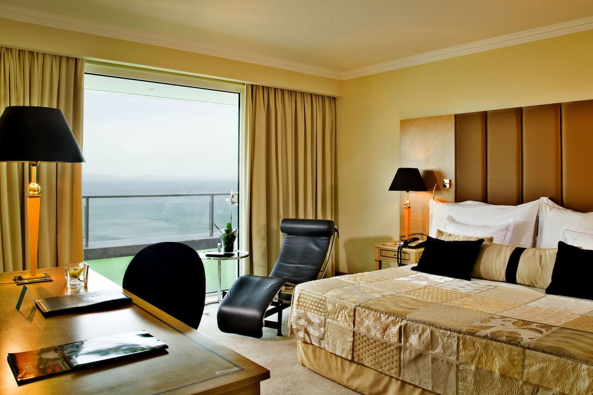 Una habitación de hotel con una cama grande, un escritorio con silla, una mesita de noche y vista al océano.