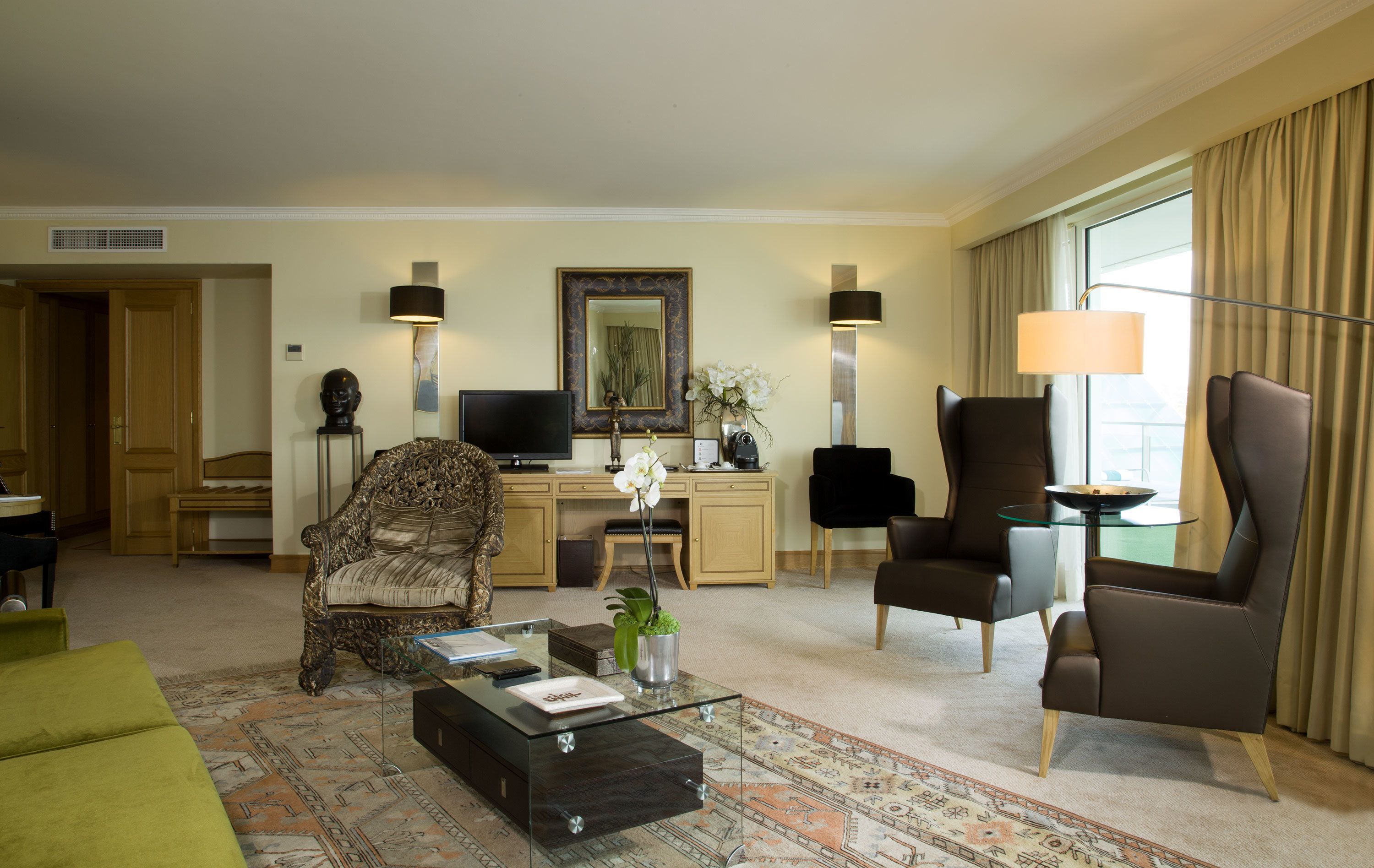 Uma sala de hotel com sofá, poltronas, mesa de centro, escrivaninha e televisão.