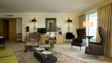 Uma sala de hotel com sofá, poltronas, mesa de centro, escrivaninha e televisão.