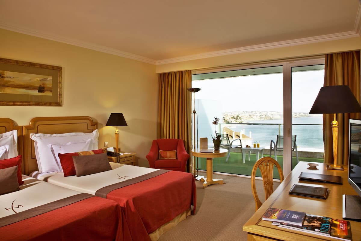 Habitación de hotel con dos camas, un escritorio, una silla, un televisor y vista al mar.