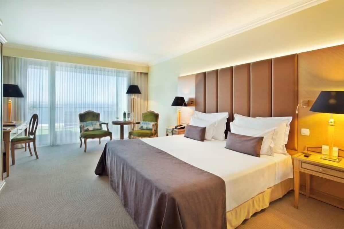 Habitación de hotel con una cama grande, dos mesitas de noche, un escritorio, una silla y vistas al exterior.