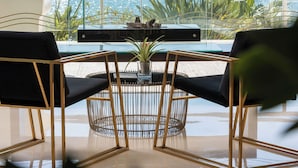 Habitación moderna con un amplio ventanal con vistas al mar, que incluye una zona de comedor con mesa y sillas, y una planta en el alféizar.