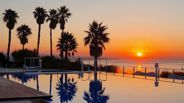 Una piscina con vista al atardecer, palmeras y una terraza de madera.