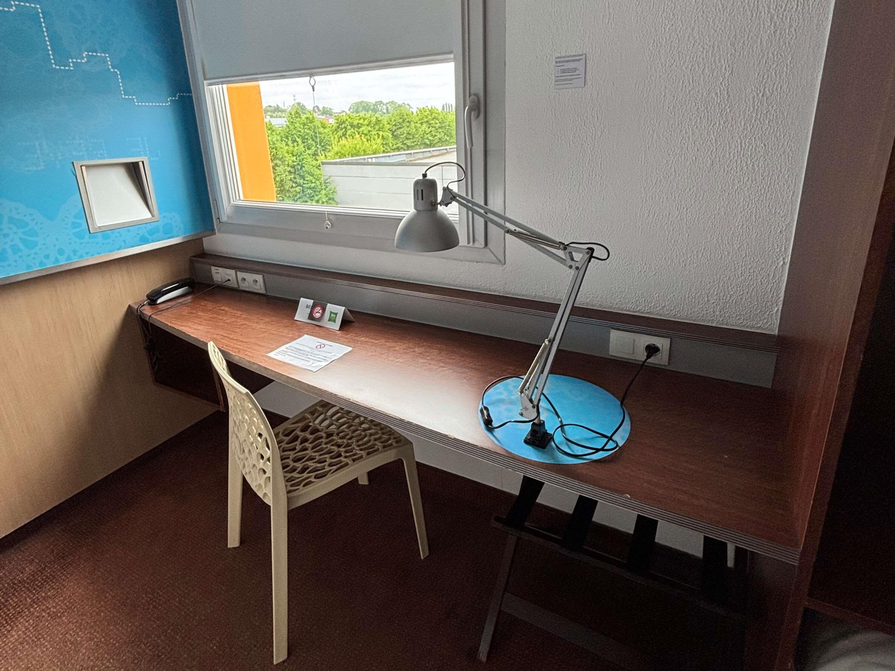 Una oficina pequeña y privada con escritorio, silla y ventana con vistas a la vegetación.