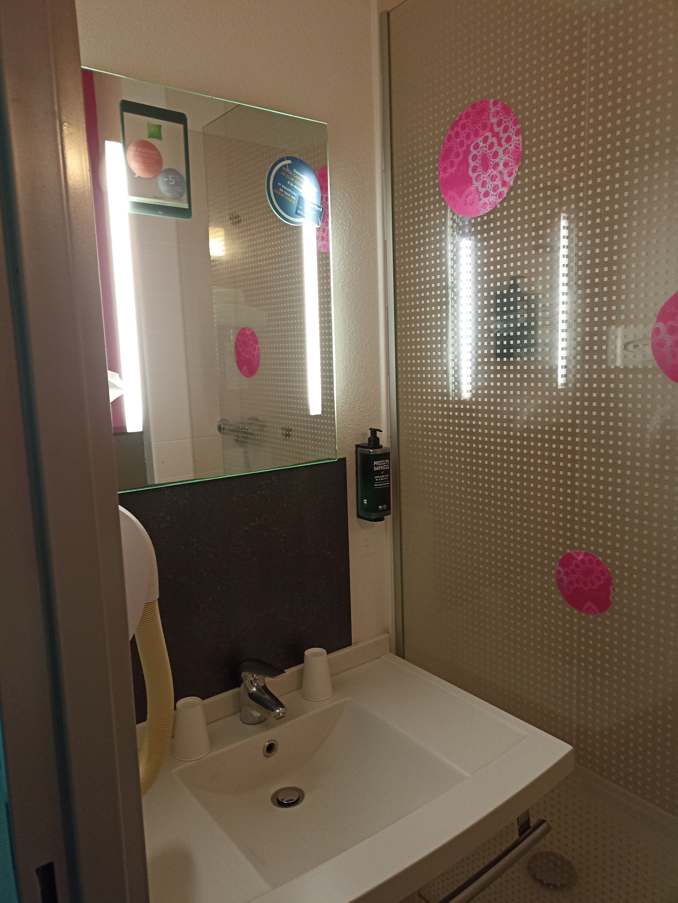 A bathroom with a white sink, a mirror, and a glass shower enclosure with pink decorative stickers.