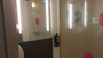 A bathroom with a white sink, a mirror, and a glass shower enclosure with pink decorative stickers.