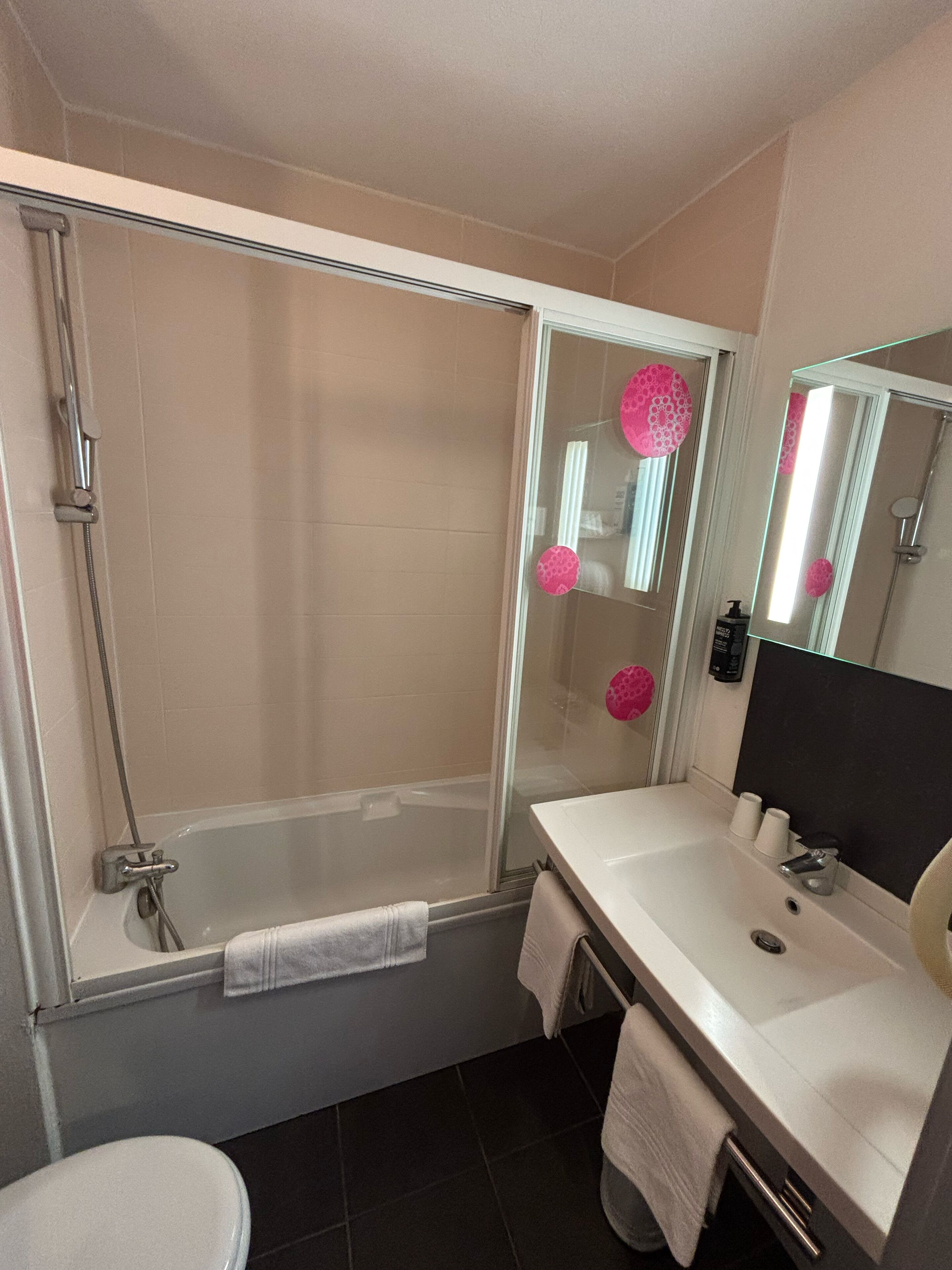 A modern bathroom with a glass-enclosed shower, a white bathtub, a sink with a mirror, and a toilet.