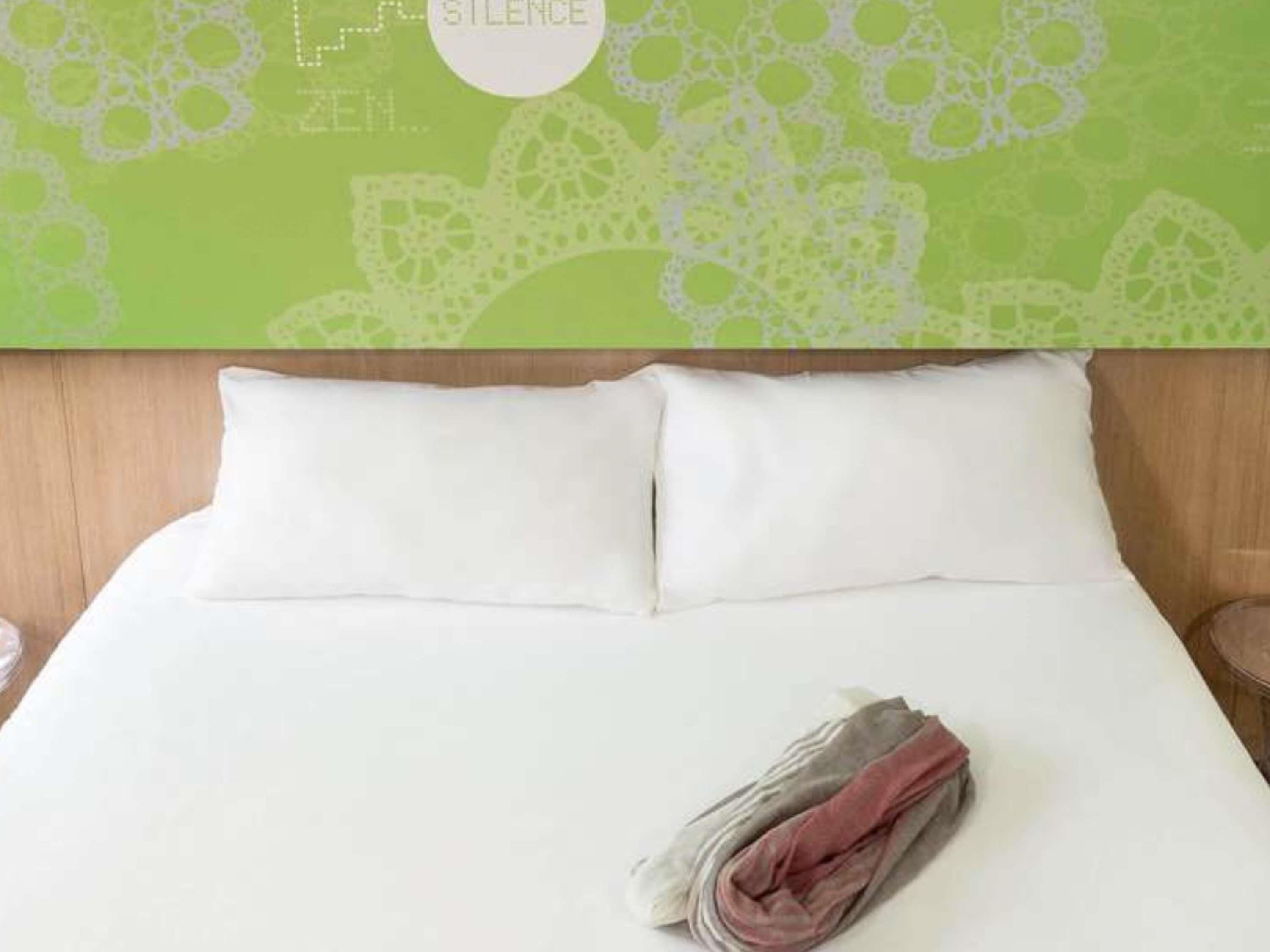 Una cama bien hecha con almohadas blancas y una manta doblada sobre un cabecero de madera.