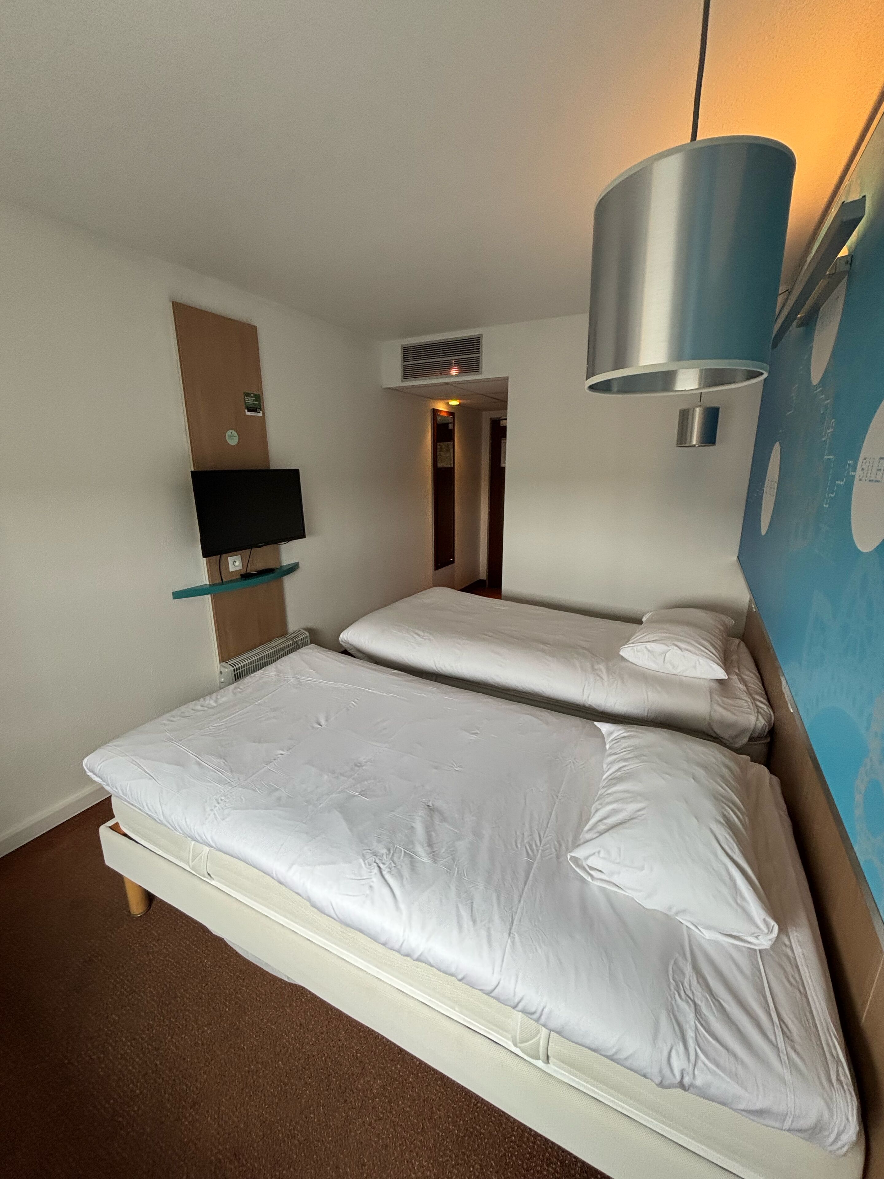 Quarto de hotel com duas camas, uma televisão fixada na parede e uma janela grande.