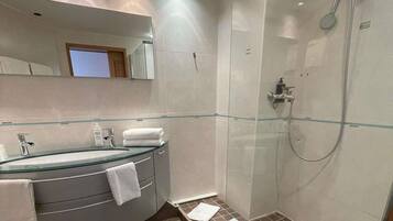 Un baño moderno con ducha de vidrio, tocador curvo con lavabo de vidrio y un espejo grande sobre el lavamanos.
