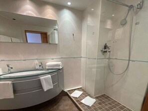 Een moderne badkamer met een douchecabine van glas, een gebogen wastafel met een glazen wasbak, en een grote spiegel boven de wastafel.