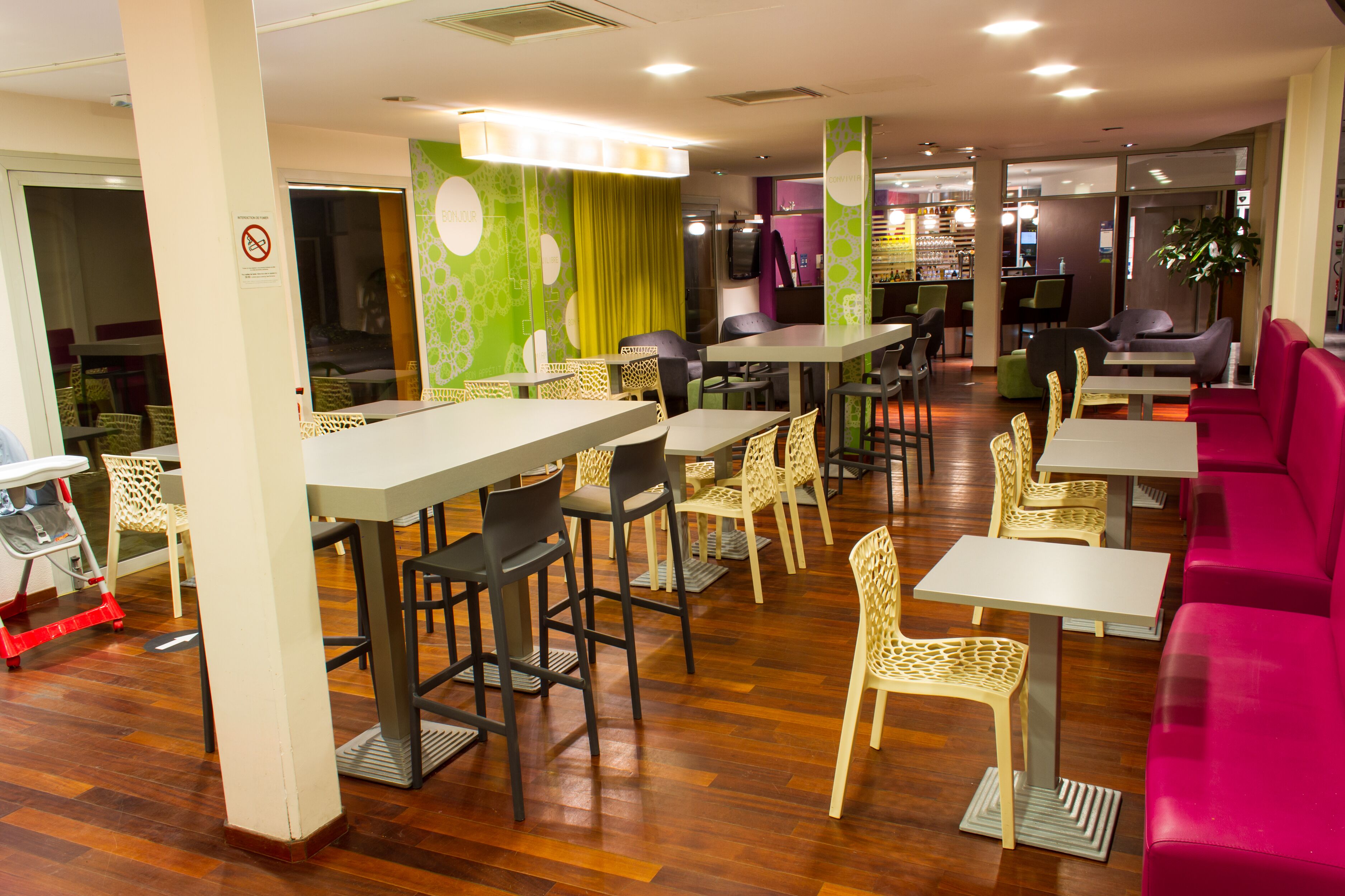 A modern restaurant with multiple seating areas, including bar stools, high tables, and cushioned chairs.