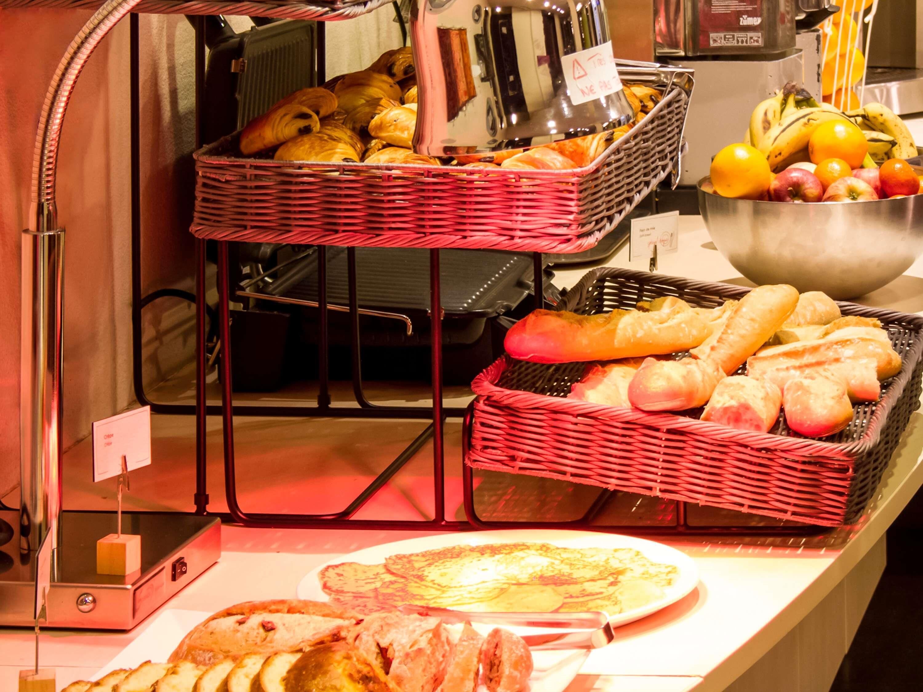 A buffet setup with baskets of bread, fruits, and a plate of pancakes.