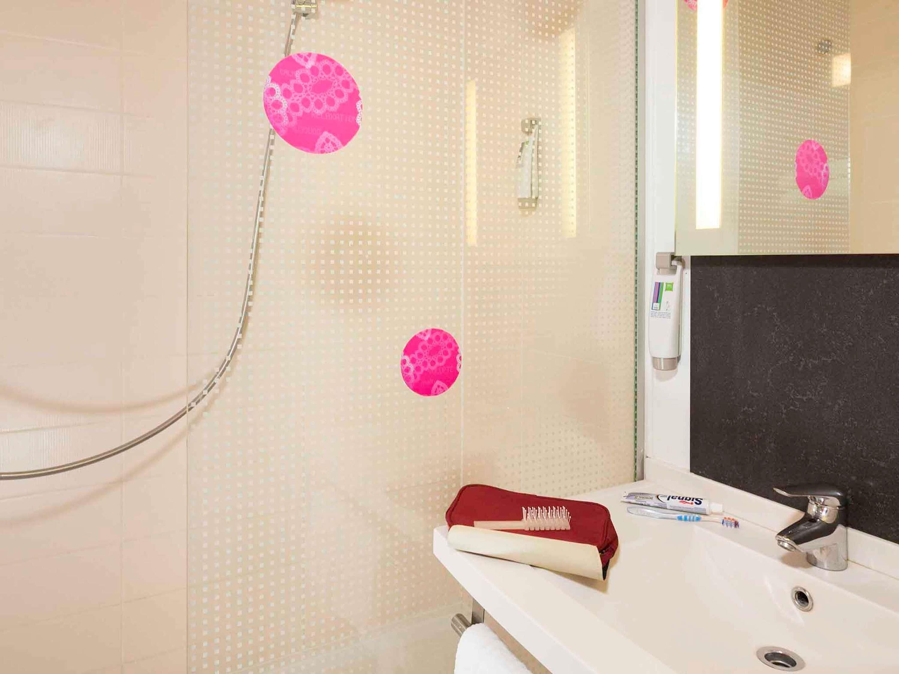 Een badkamer met een douche, wastafel en spiegel.