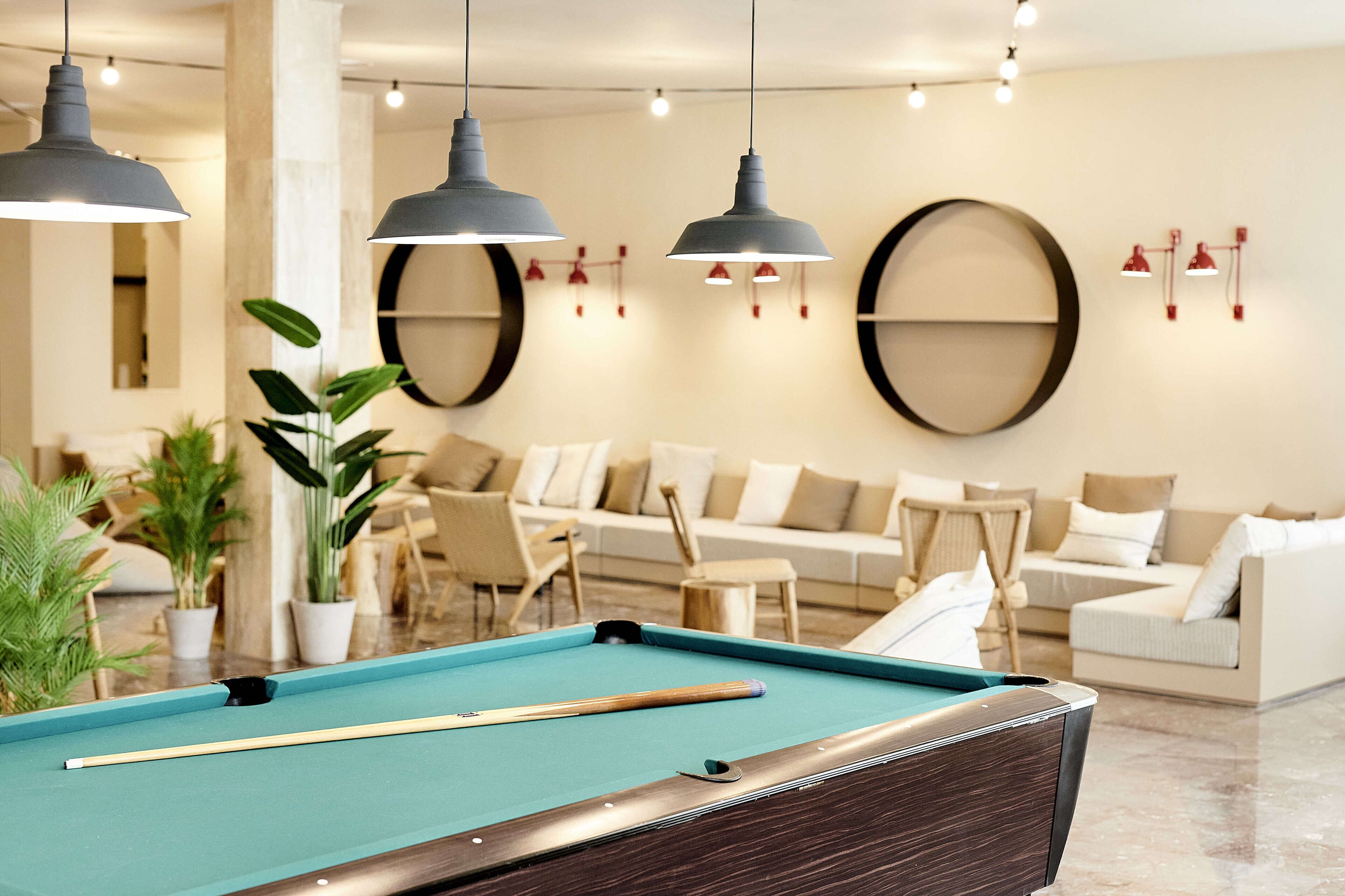 A pool table with a pool cue and a billiard ball, surrounded by a modern living area with sofas and a coffee table.