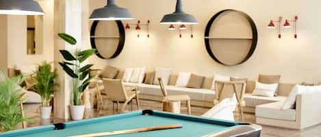 A pool table with a pool cue and a billiard ball, surrounded by a modern living area with sofas and a coffee table.