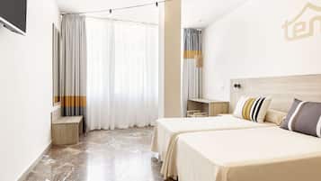 A hotel room with two beds, a TV, a desk, and a large window with curtains.