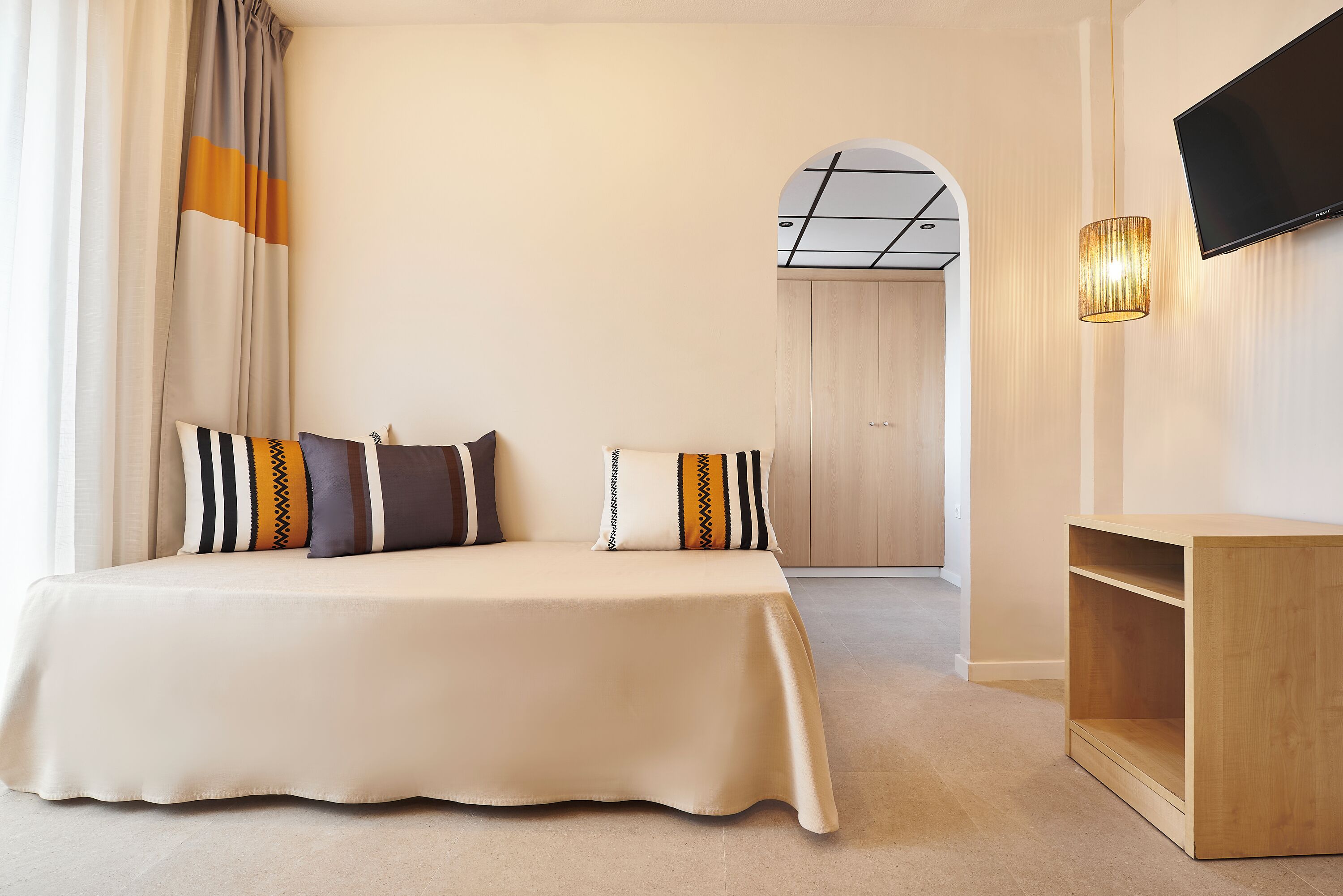 Habitación de hotel con una cama grande, un televisor montado en la pared y una mesita de noche de madera.