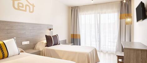 Ein Hotelzimmer mit zwei Betten, einem Schreibtisch, einem Fernseher und einem großen Fenster mit Vorhängen.