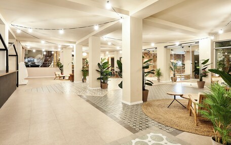 A spacious lobby with a modern design, featuring a central seating area, potted plants, and a staircase leading to upper floors.