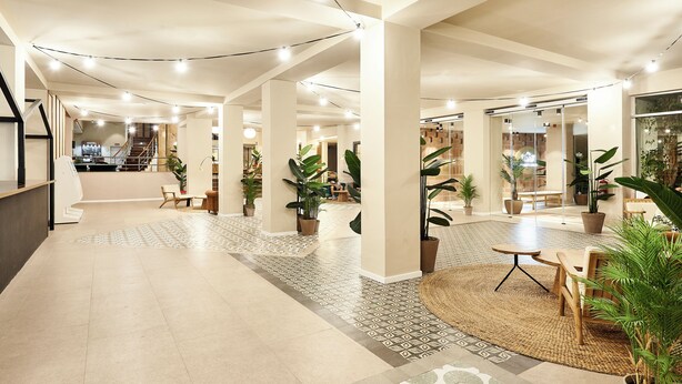 Un hall d’entrée spacieux au design moderne, comprenant un espace salon central, des plantes en pot et un escalier menant aux étages supérieurs.
