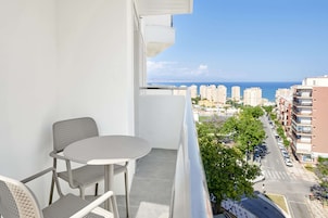 Een balkon met een tafel en stoelen, met uitzicht op een kustplaats met gebouwen en een heldere lucht.