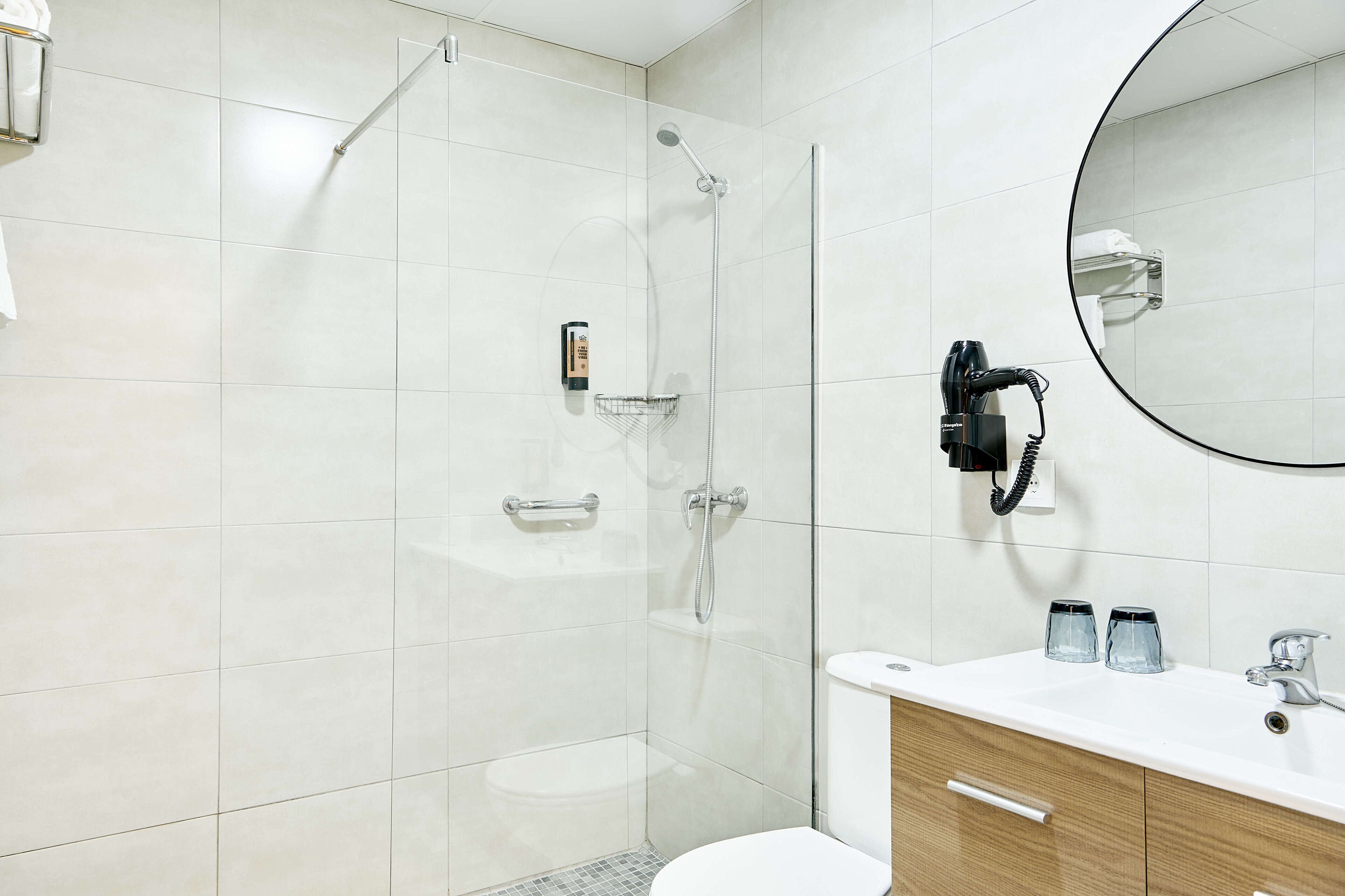 A modern bathroom with a glass-enclosed shower, a toilet, and a vanity with a mirror and two glasses.