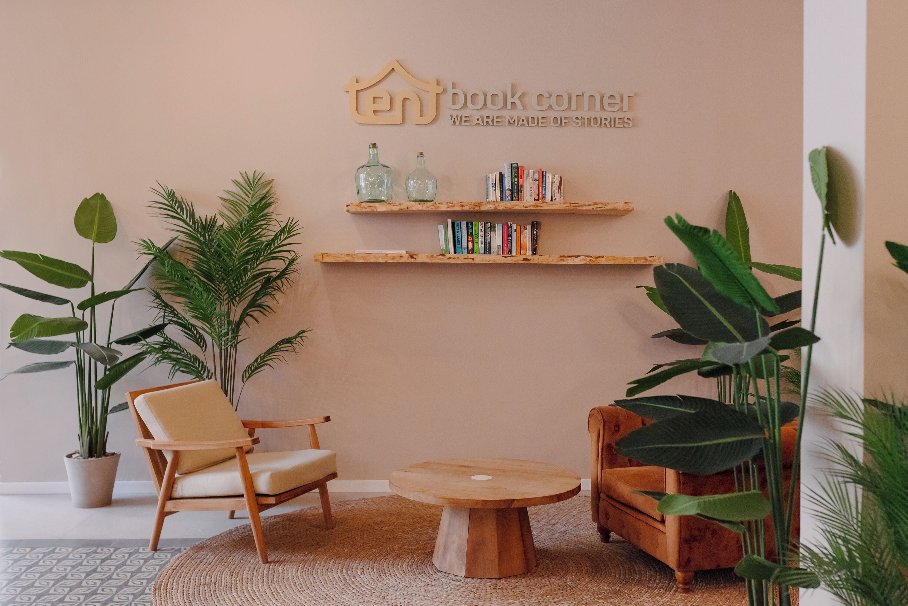 A cozy reading nook with a round wooden table, two chairs, and a bookshelf against a peach-colored wall.